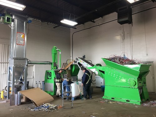 Workers collecting copper scrap granules from wire recycling machine